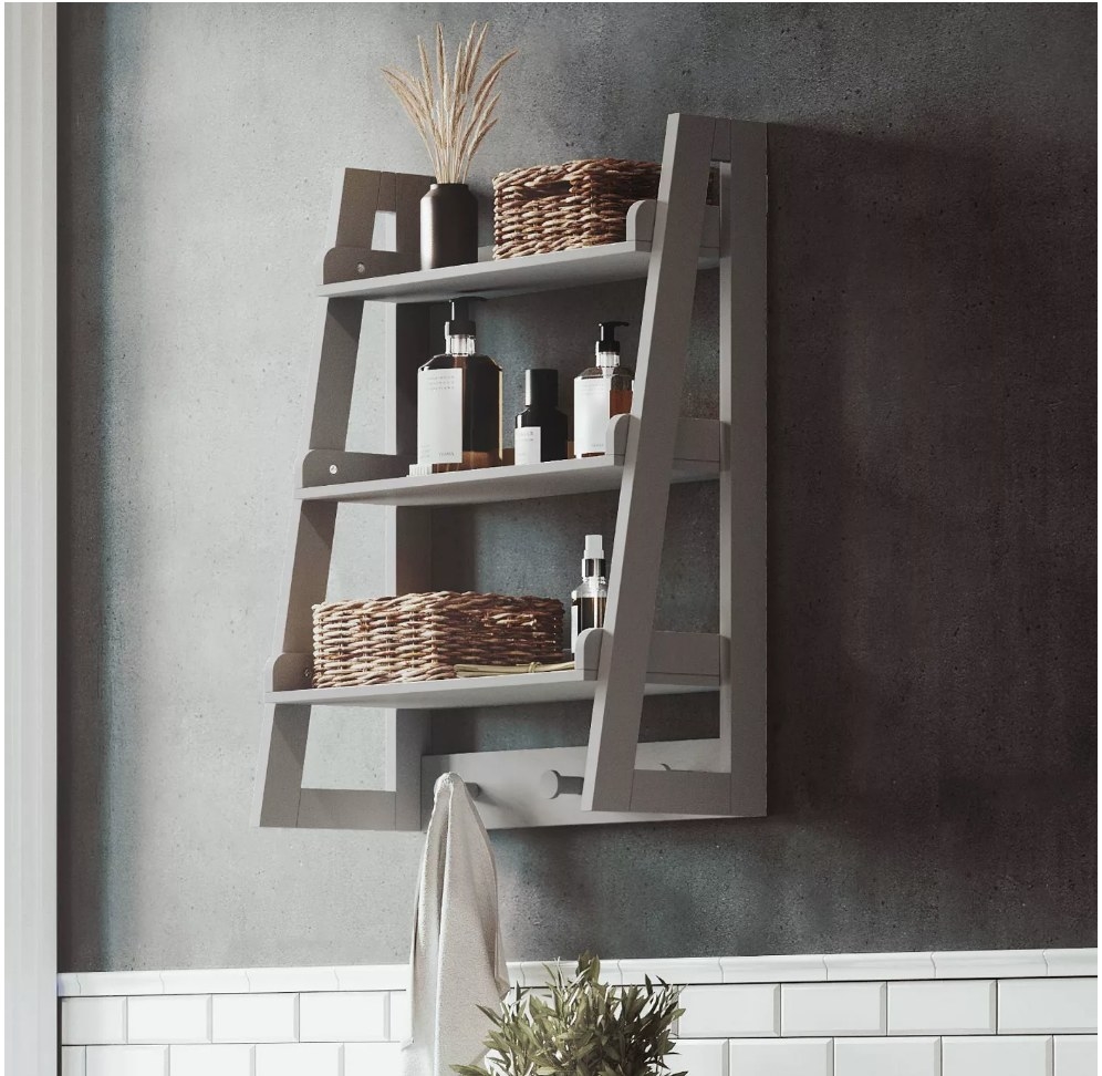 A gray, wall-mounted 3-tier ladder shelf with 3 hooks for towels displayed in a bathroom