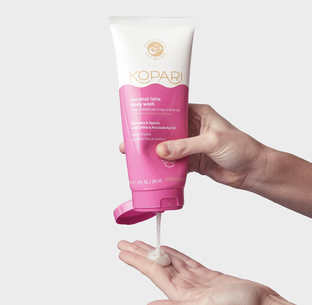 A model squeezing coconut latte body wash into their hands from a bottle 