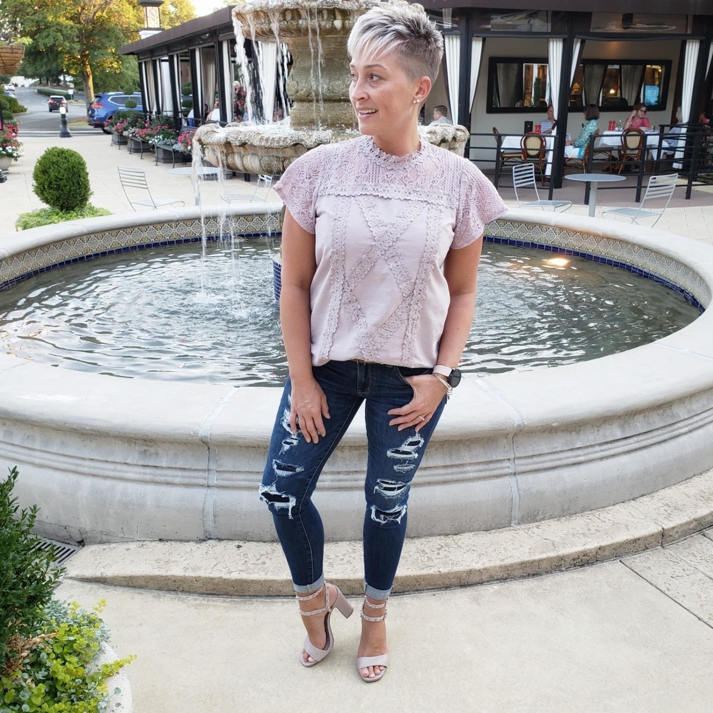 reviewer wearing the purple lace blouse with dark blue jeans and heeled sandals outside