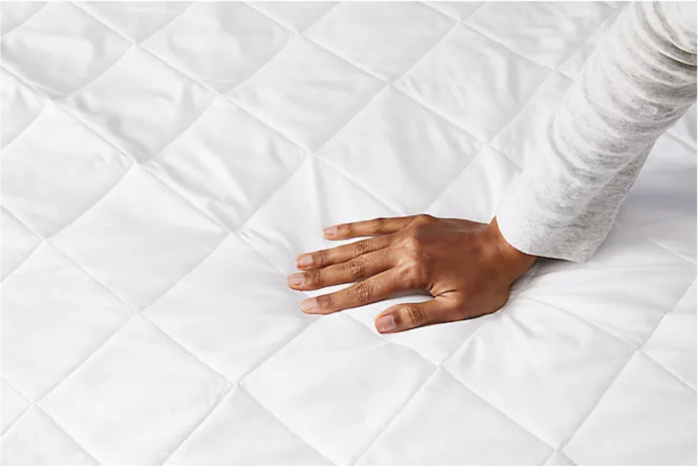 Model pressing hand into quilted white mattress pad 