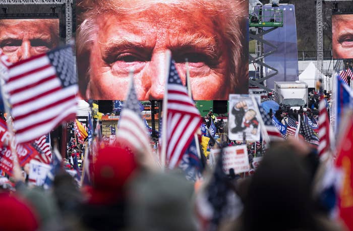 A close-up of Trump&#x27;s eyes appear on three video screens playing in front of a crowd wearing red caps and waving US flags and Trump flags