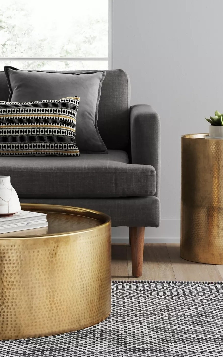 A cylindric gold accent table in a living room with a hammered exterior