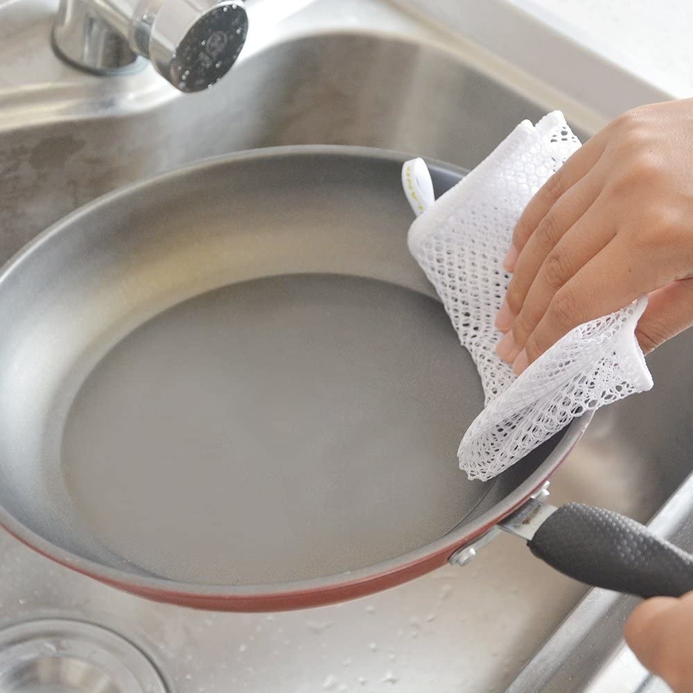 A person scrubbing a pan with a mesh dish cloth