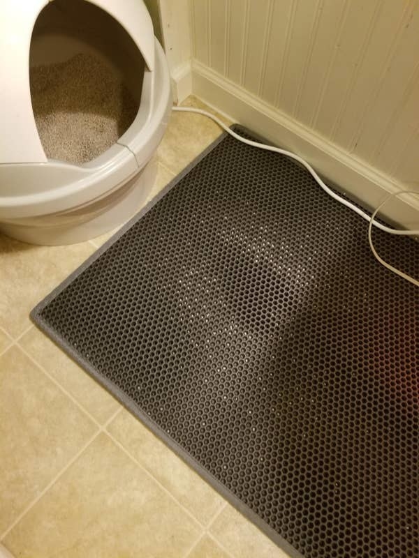 A reviewer shows off how much litter their gray mat caught when placed in front of their litter box (it&#x27;s a lot!)