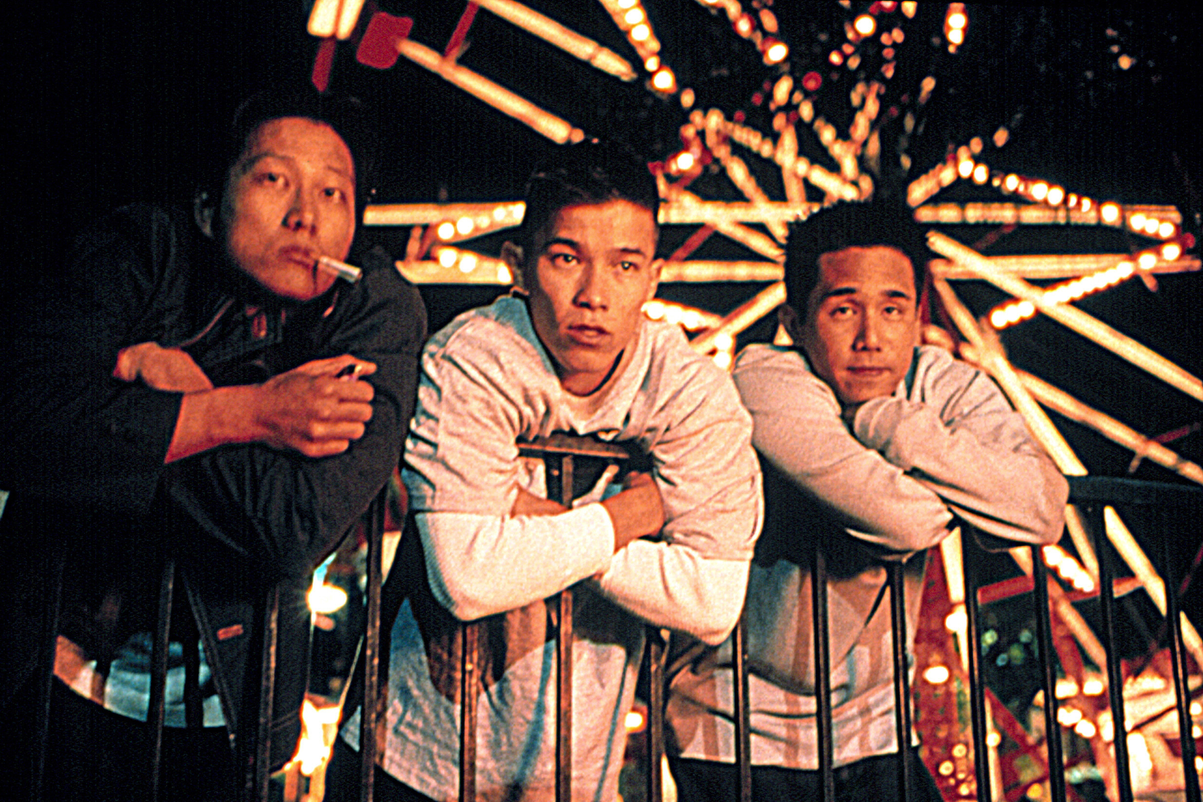 Three men leaning on a fence in front of a Ferris wheel