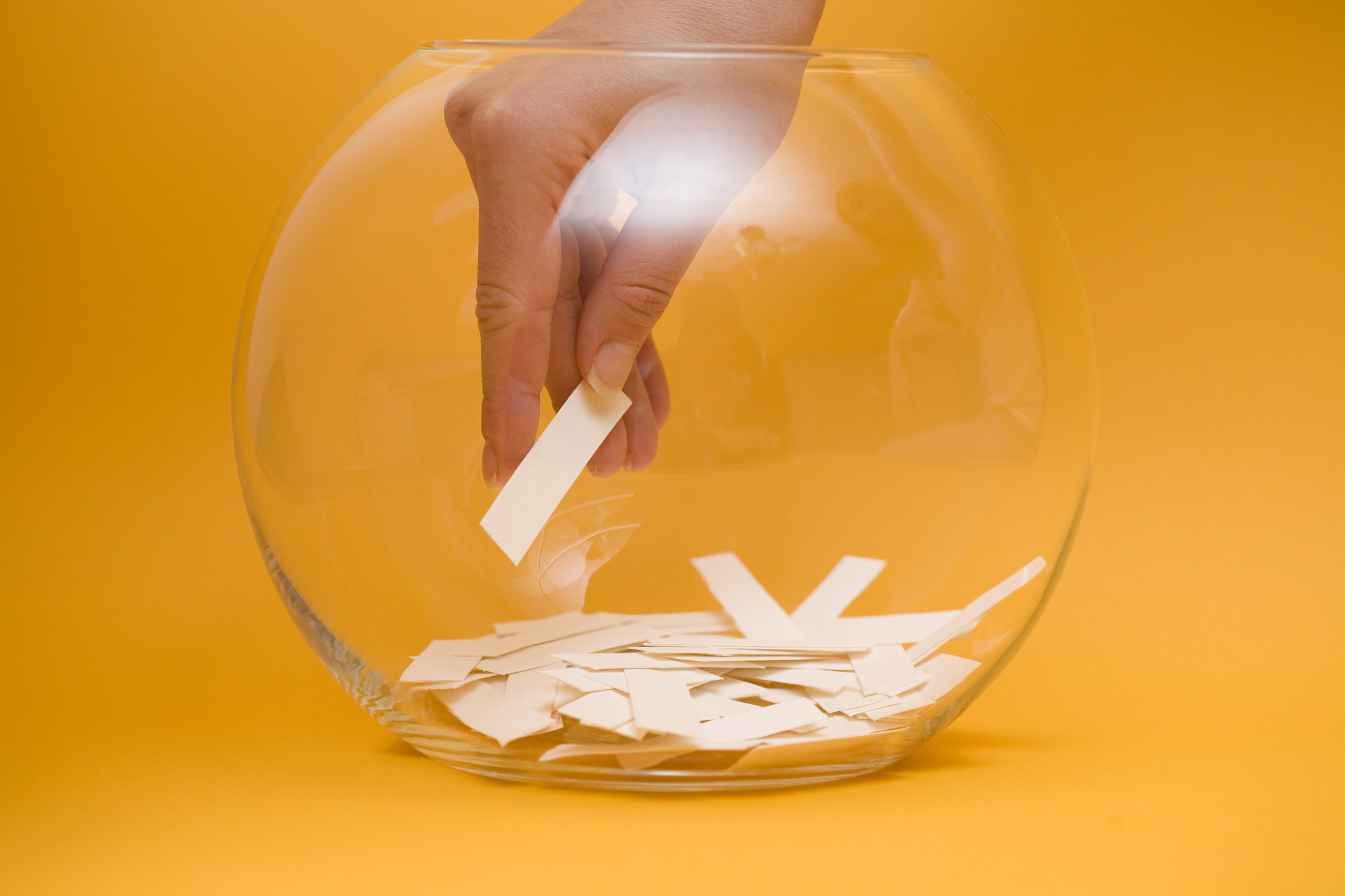 A hand reaching into a clear bowl to pick a lottery winner