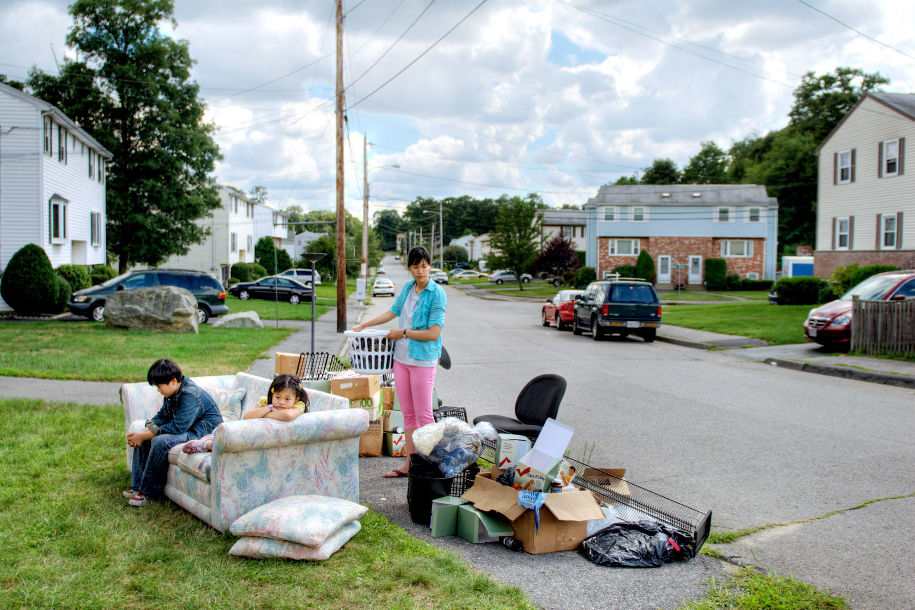 Two children and a mother sitting outside on a couch among their belongings