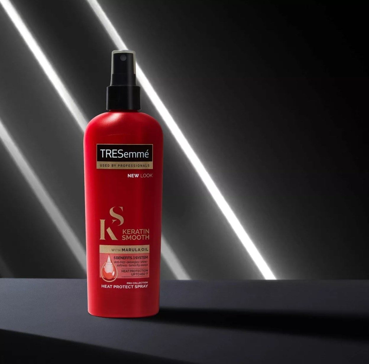 Red bottle of Tresemme heat styler against grey-black background