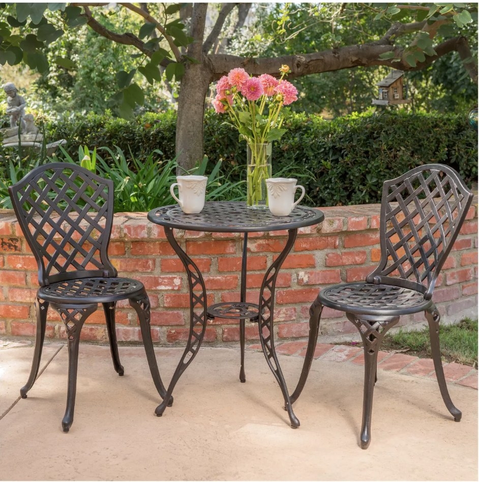 A black and bronze bistro set with two chairs and a table displayed in a garden