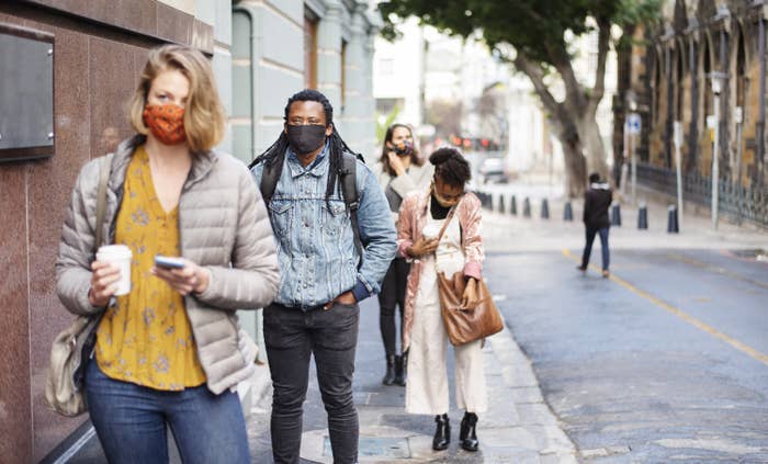 A group of people walking on the side walk, all wearing masks