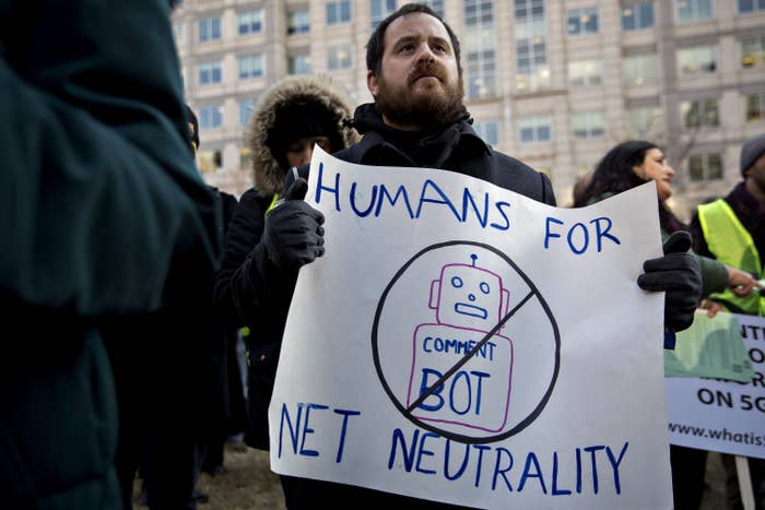 A demonstrator holds a poster that says &quot;Humans For Net Neutrality.&quot; The poster also contains a drawing of a robot, crossed out and with &quot;Comment Bot&quot; written on its torso.