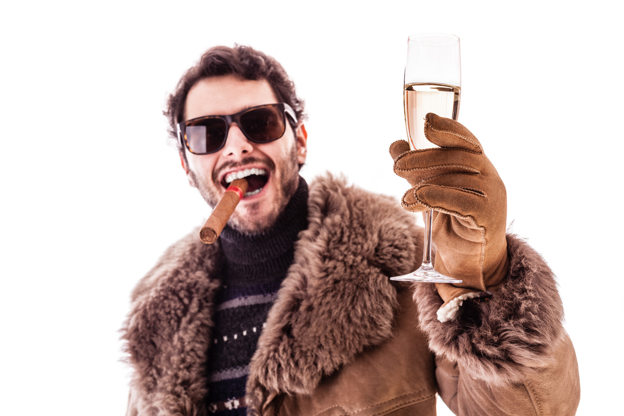 a young man wearing a sheepskin coat isolated over a white background holding a cigar and a glass with champagne