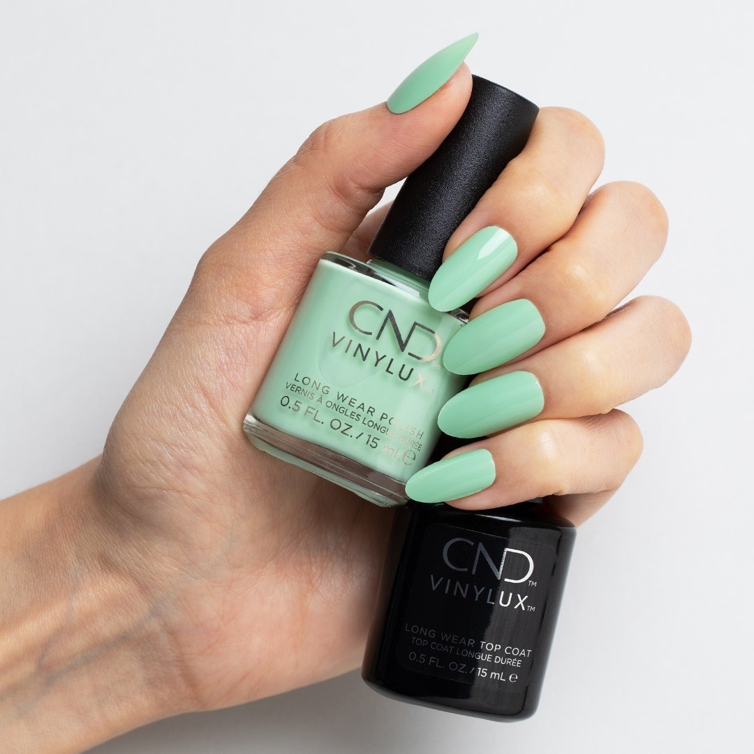 Hands holding CND top coat and mint green polish, nails painted mint green