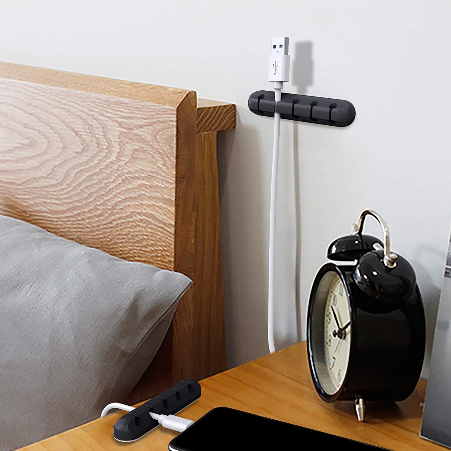 A cable clip on a wall behind a bed and one on the bedside table