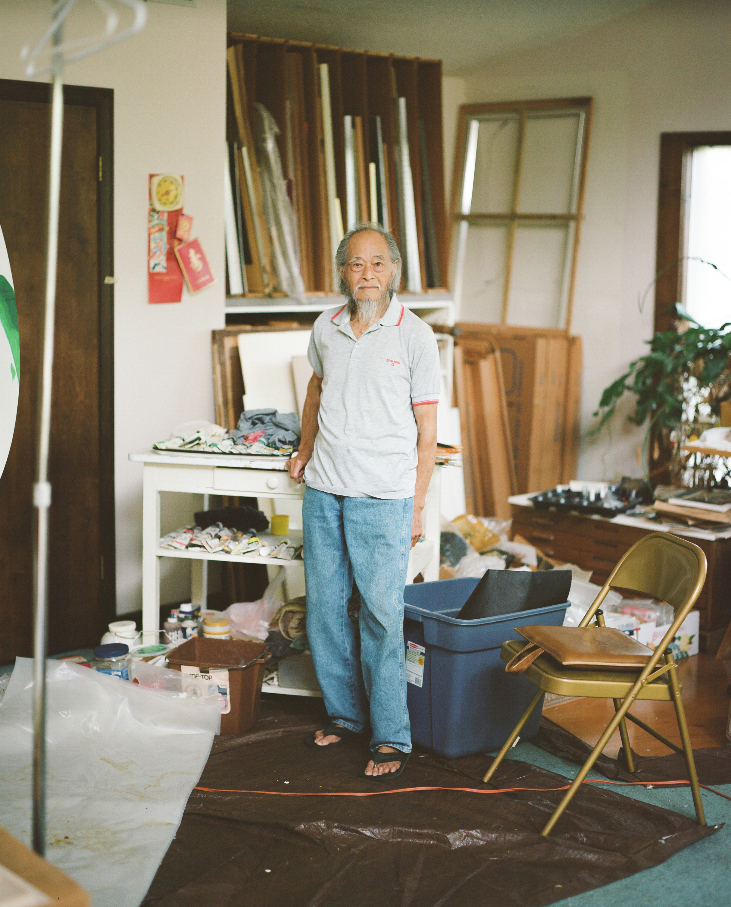 An older man in jeans and flip flops stands in a studio