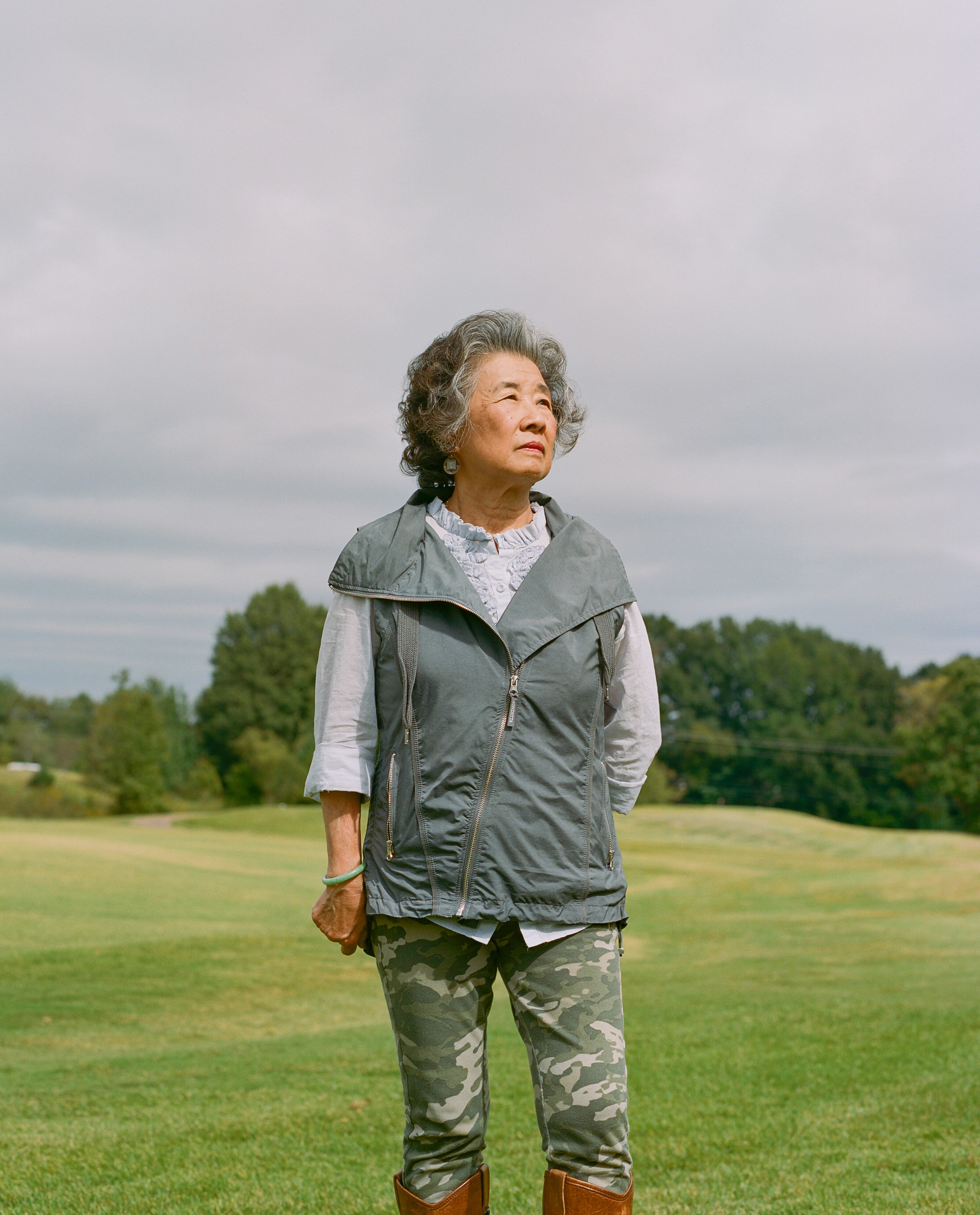 An older woman stands in a field wearing camo pants