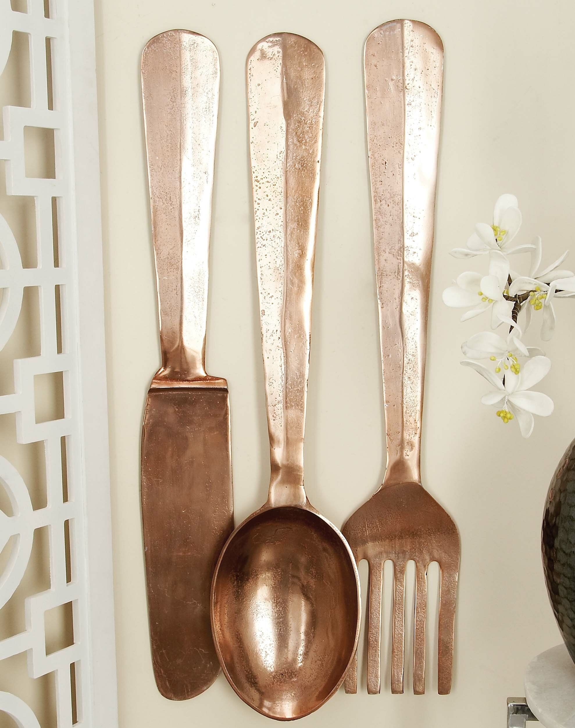 A copper fork, spoon, and knife with textured handles hanging on a wall