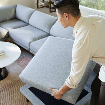 a model placing a cushion on a grey couch