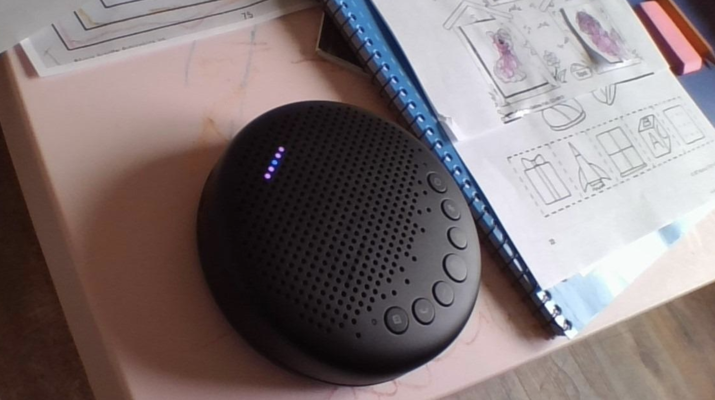 A small round black speaker with buttons controlling volume and settings on a desk 