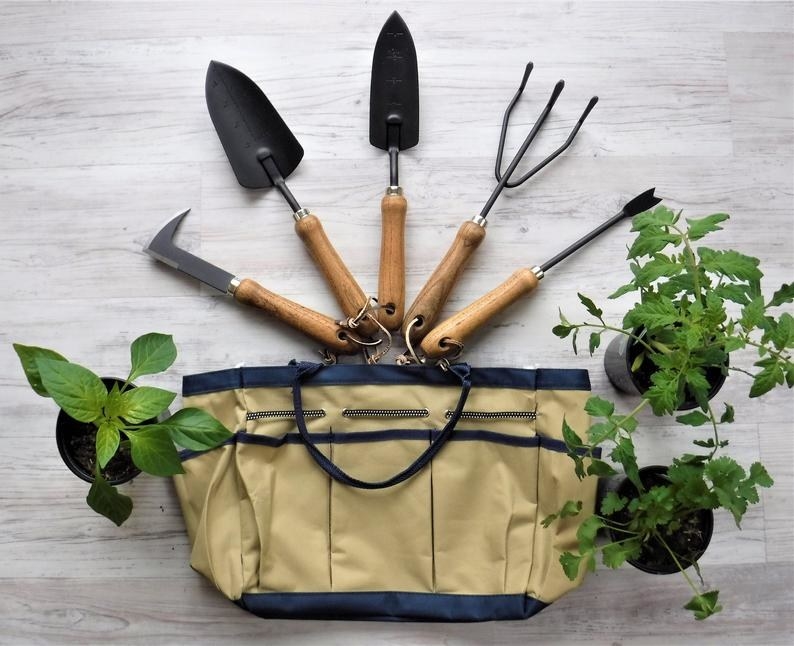 the five garden tools attached to a key ring above the gardening bag, surrounded by plants
