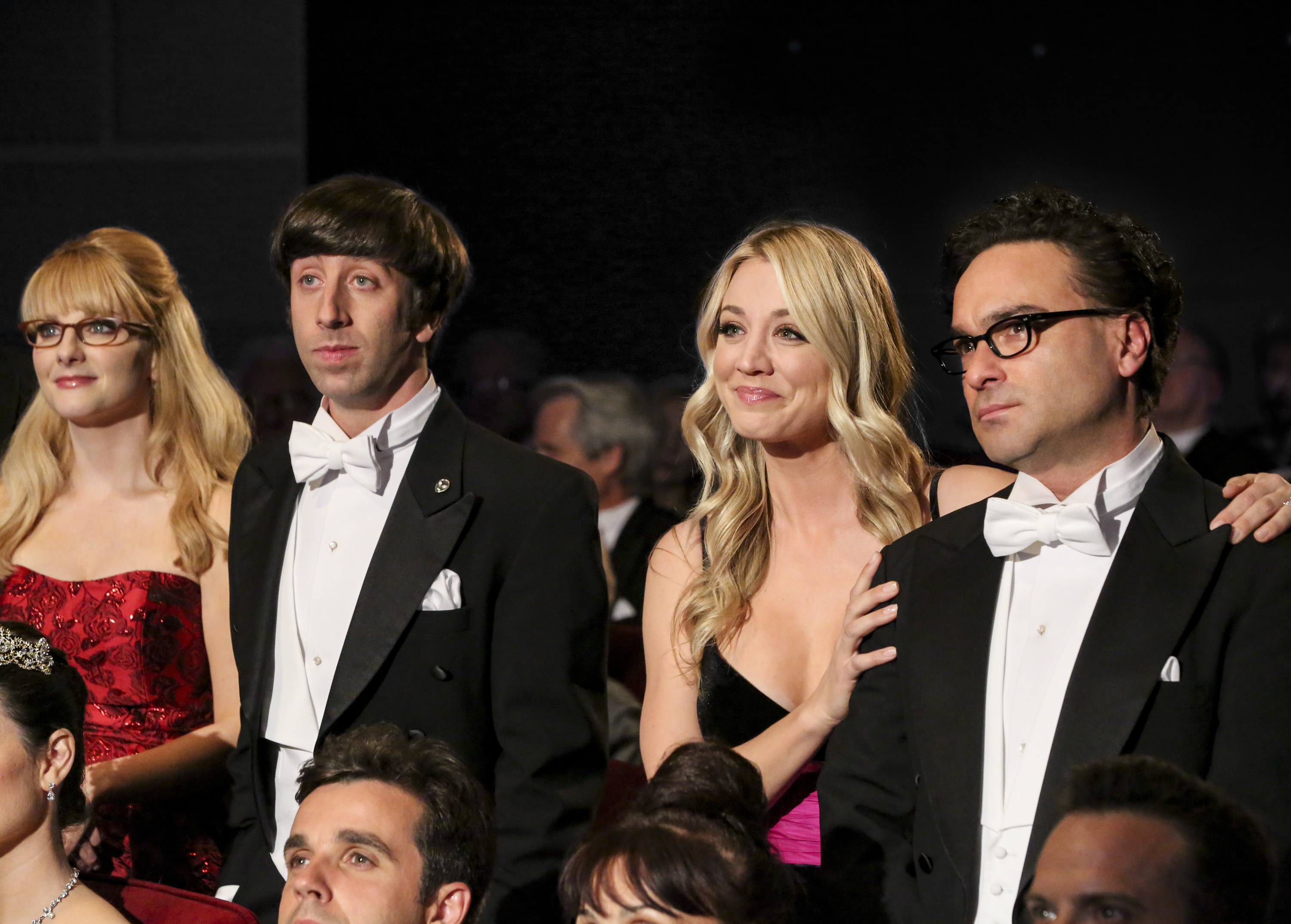 Leonard, Penny, Howard, and Bernadette stand in the audience at a black-tie event