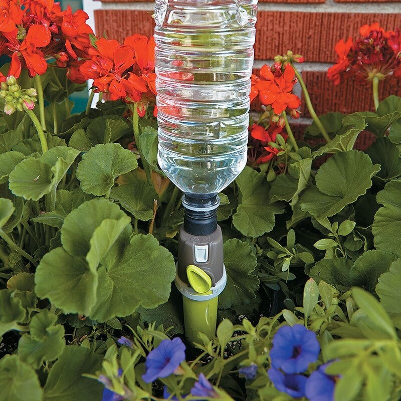 A drip spike inserted into a garden bed and topped with a full water bottle