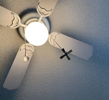 A reviewer's ceiling fan with the ball chains attached, one with a lightbulb shaped pull and one with a fan shaped pull