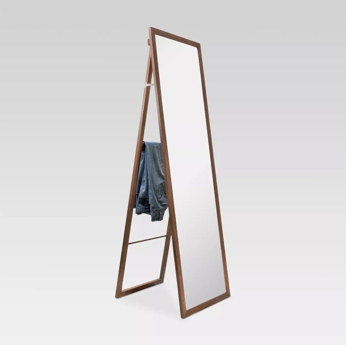 The brown wooden mirror has a pair of jeans laying on the ladder portion