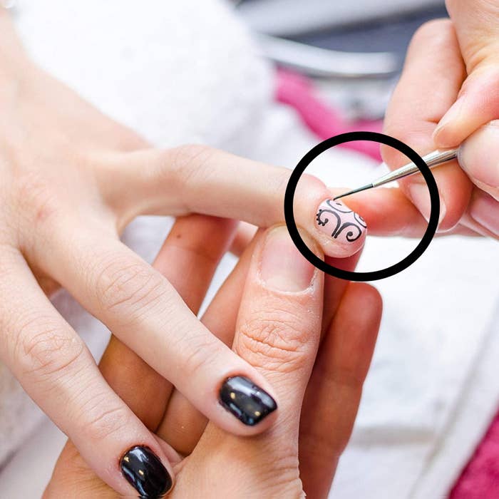 A person drawing intricate lines onto a finger nail with one of the brushes