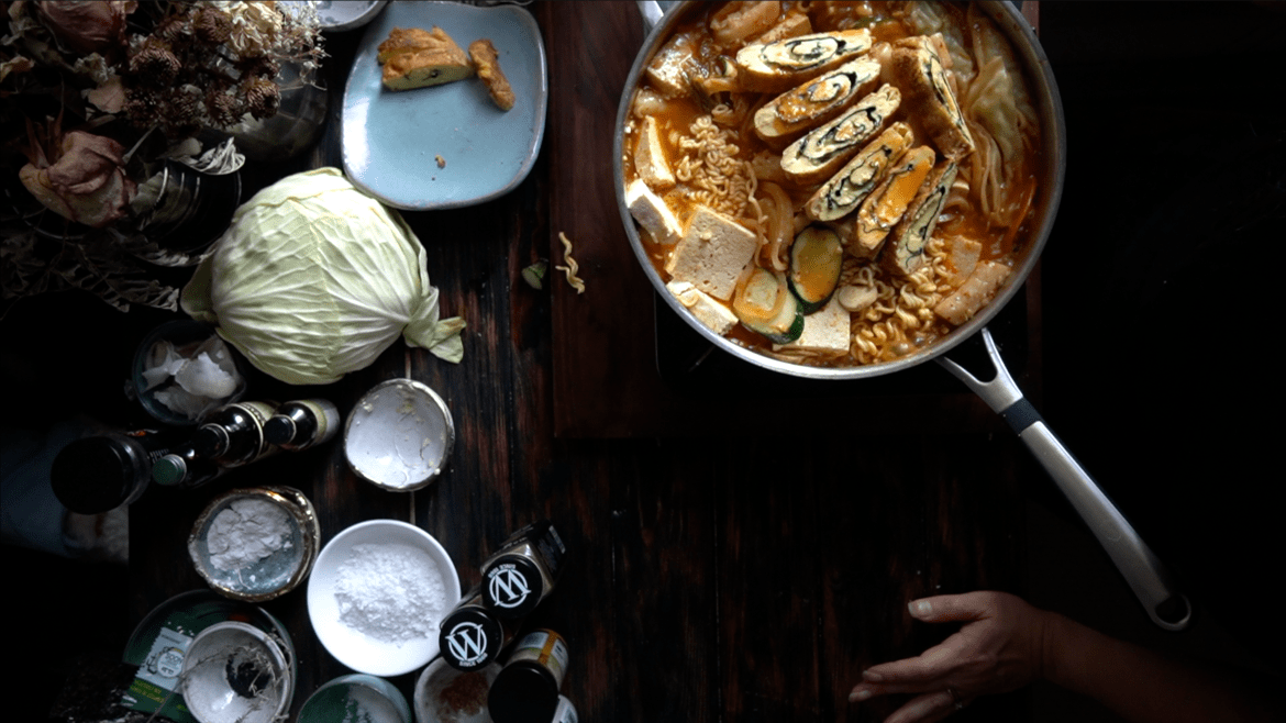 a dark and intriguing table with cabbage, salt, and other ingredients next to the budae chigae