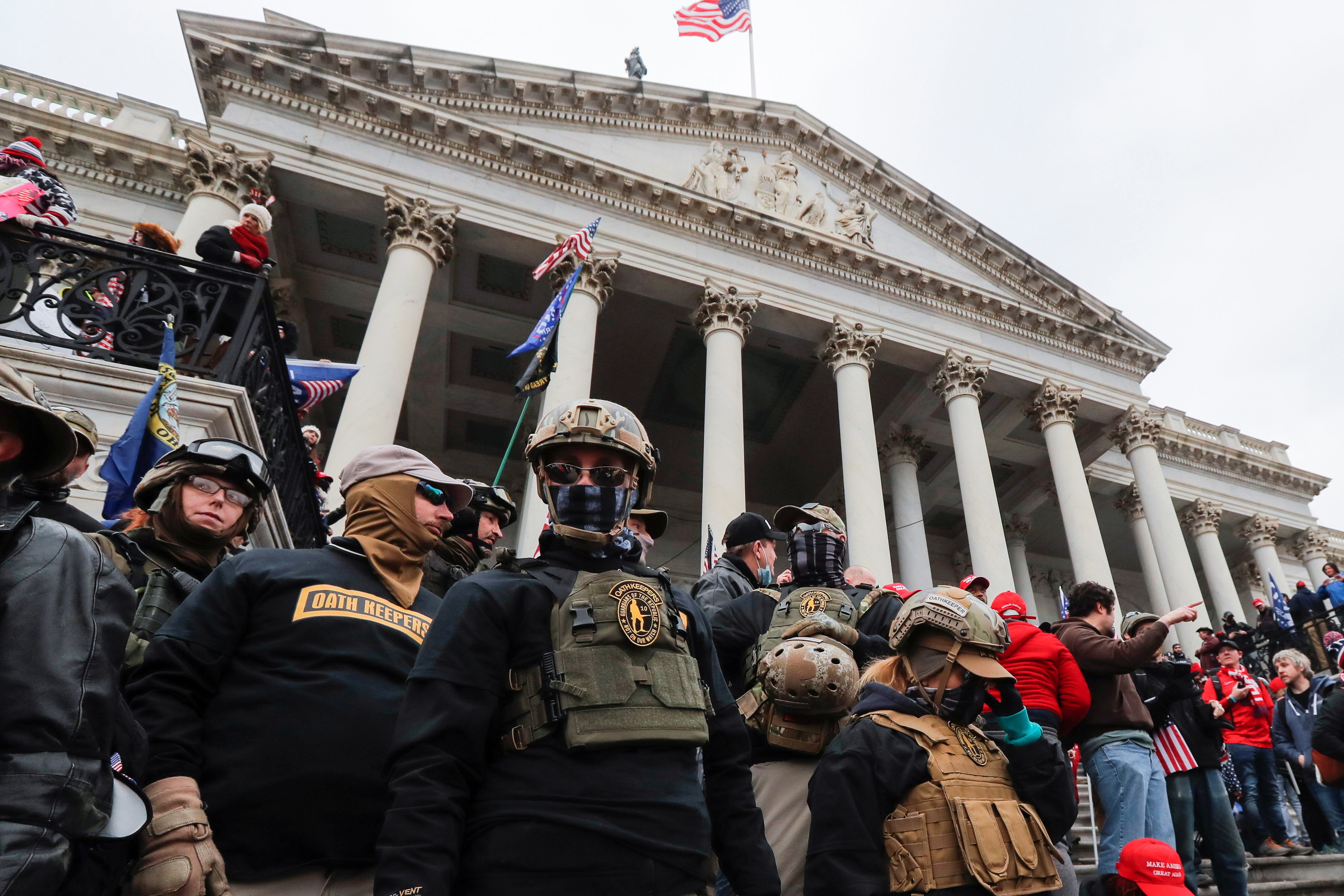 People wearing military-style tactical gear stand among a crowd outside the Capitol building in DC