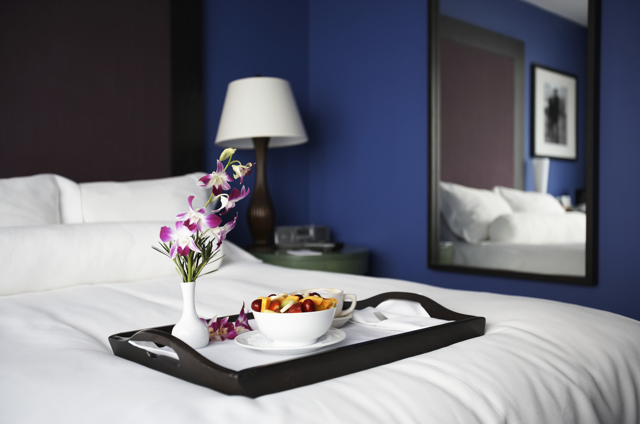 Breakfast on tray on bed in hotel room with mirror on wall in the background