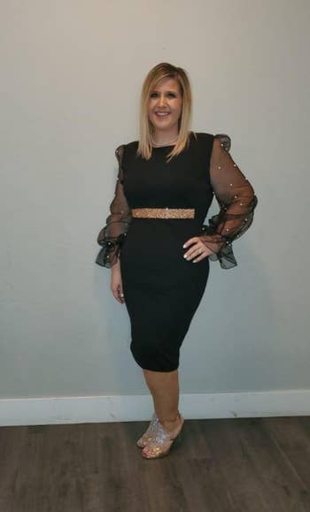 Reviewer in black fitted dress with sheer sleeves