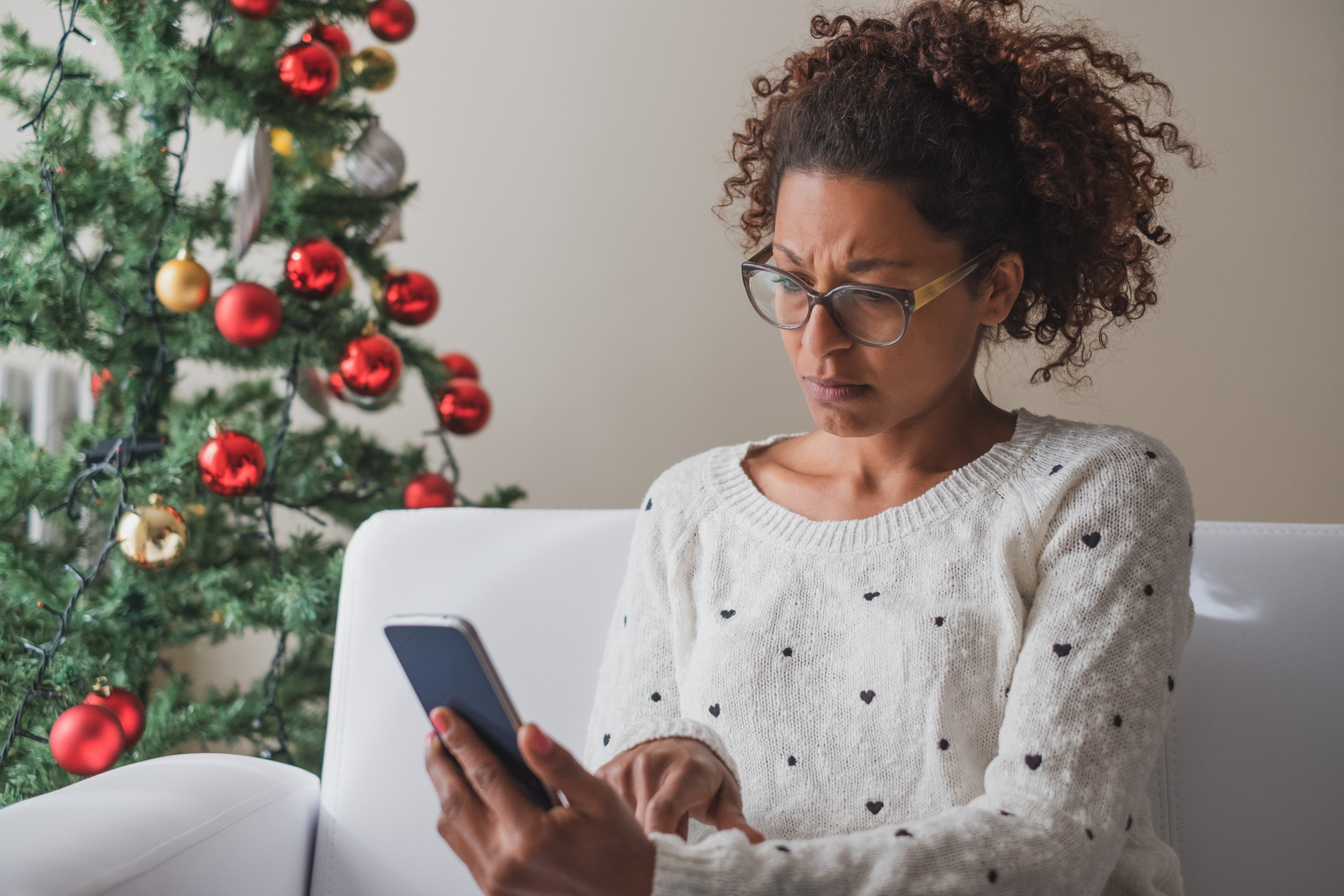 Woman looking at her phone next to Christmas tree