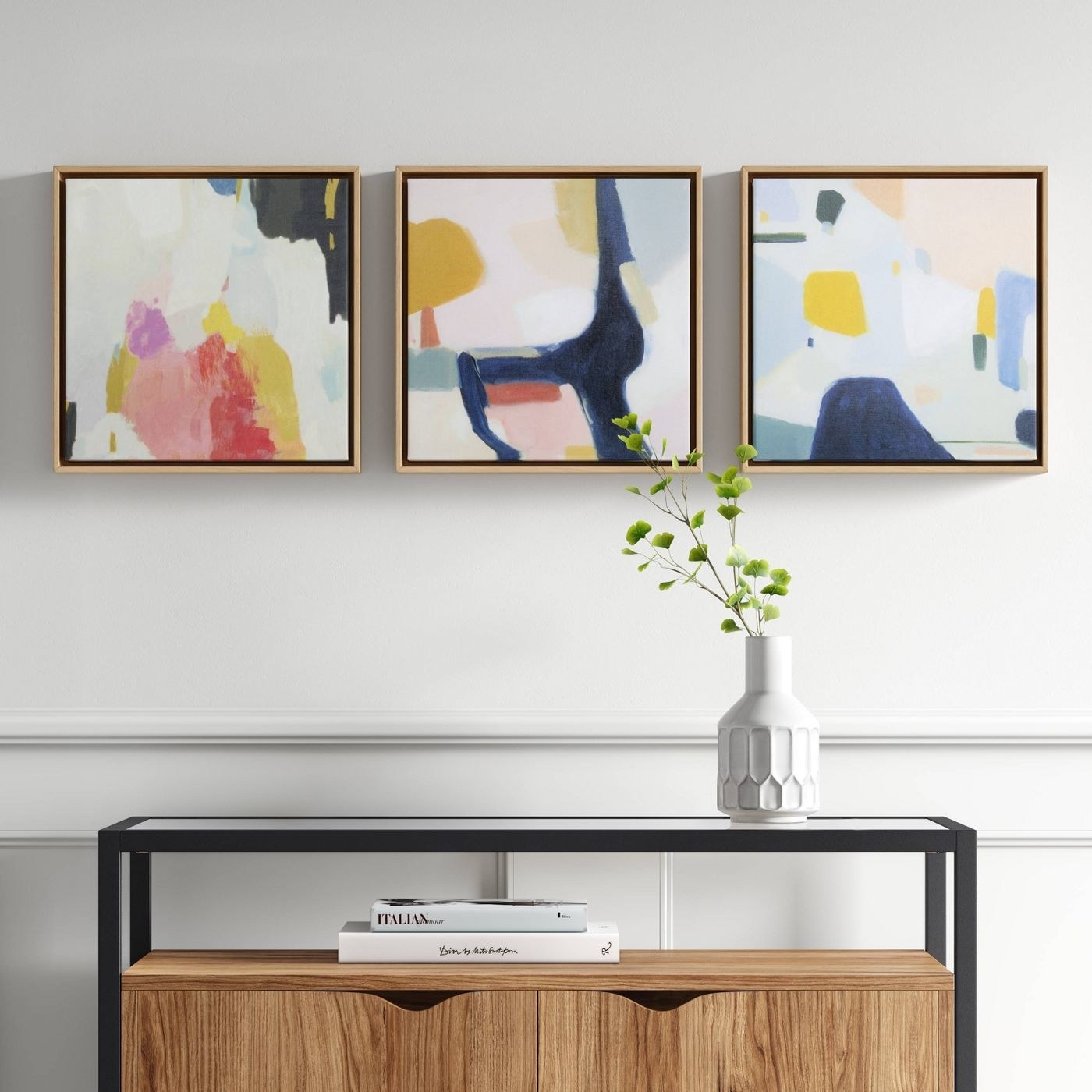 A set of three framed canvas abstract paintings above a console table