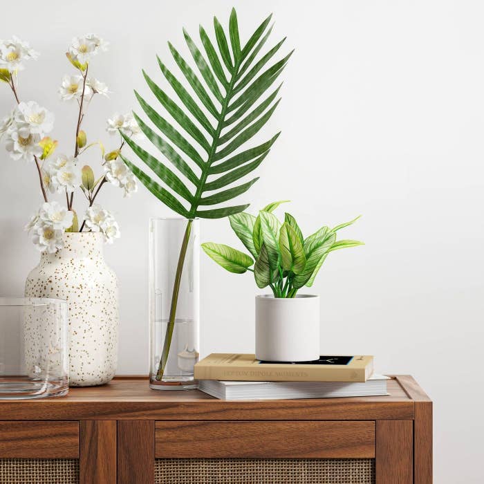 An artificial plant in a white pot on top of a console table