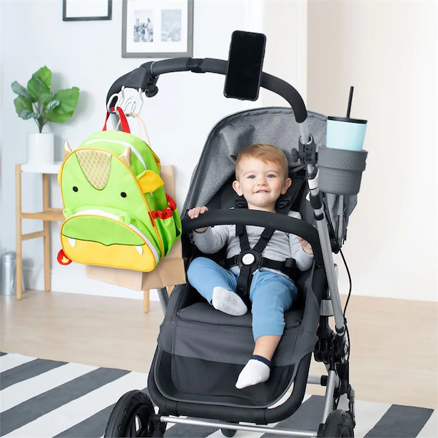 A baby sitting in a stroller with a phone attached to the handle