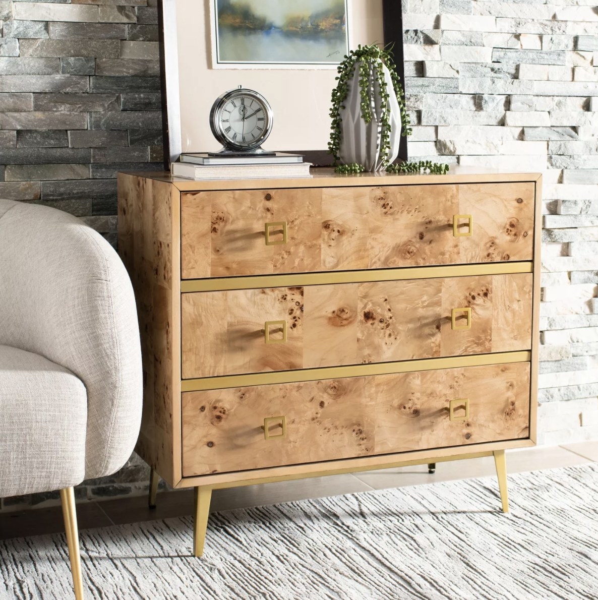 A light brown dresser with gold handles and detailing in a gray room