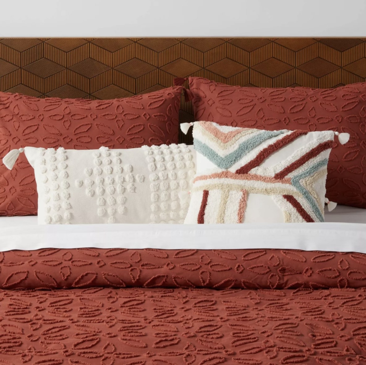 The pillow with blue, taupe, maroon and pink detailing is on top of a deep reddish-brown comforter