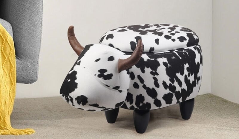 Black and white cow print ottoman shaped like a cow with a head and horns and with storage lid