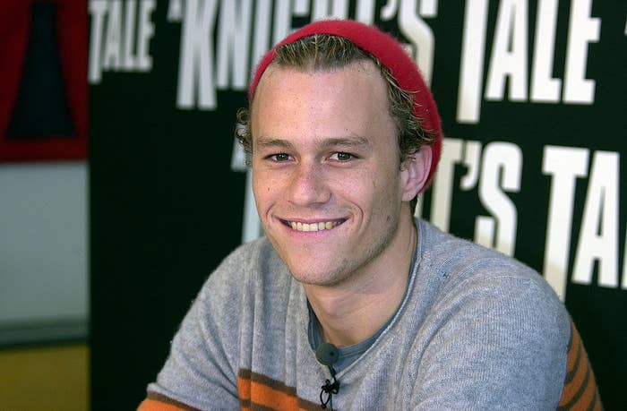 Heath Ledger sitting down during a press conference and smiling at the camera