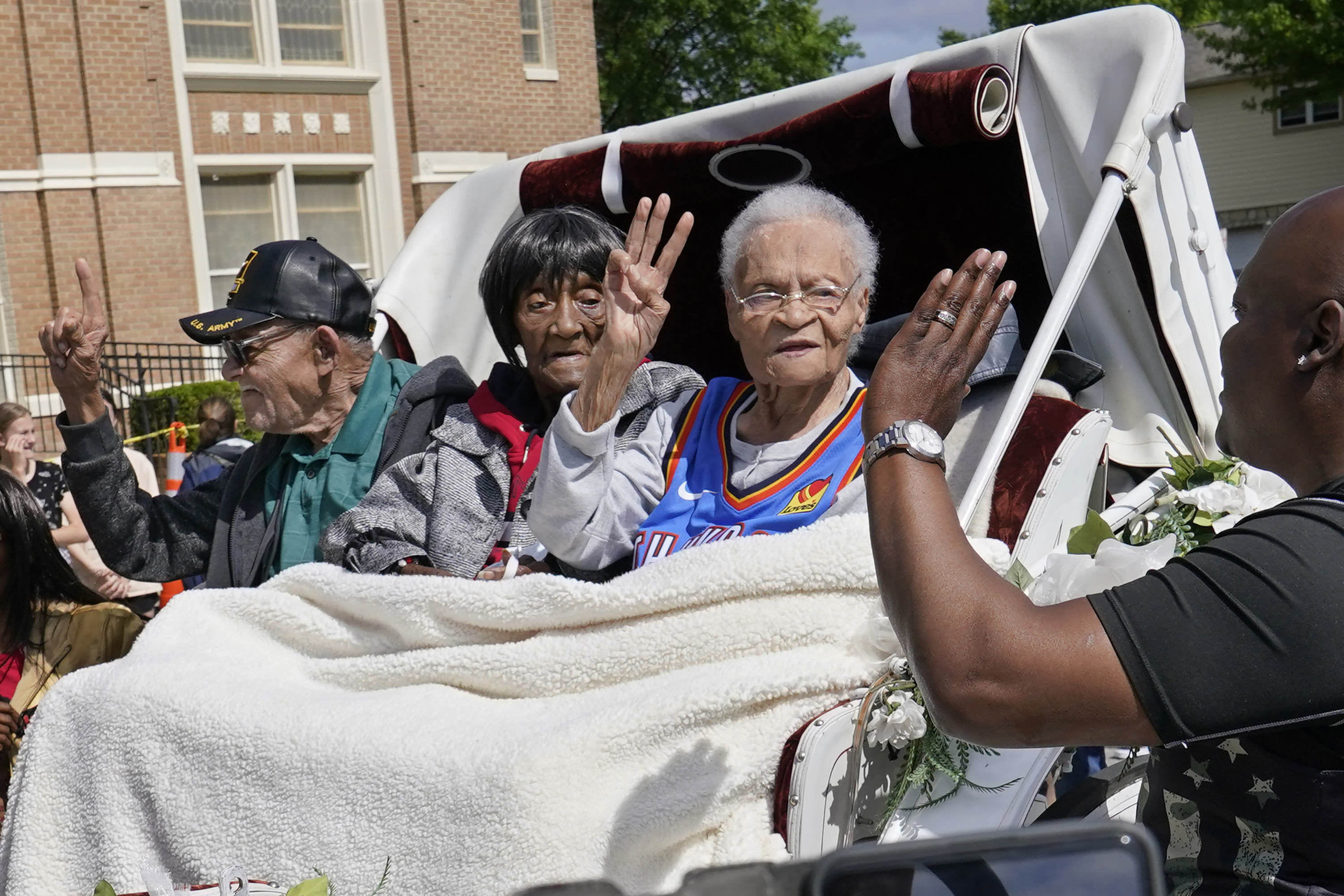 An older Black man and two older Black man wave as they sit in the back of a carriage