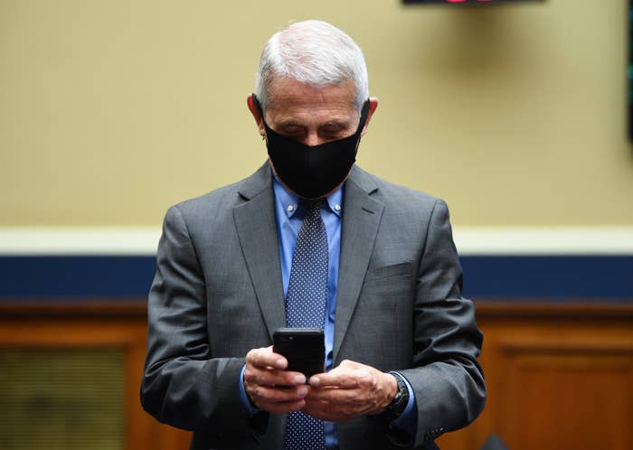 Anthony Fauci, wearing a face mask, looks down at his cellphone in his hands