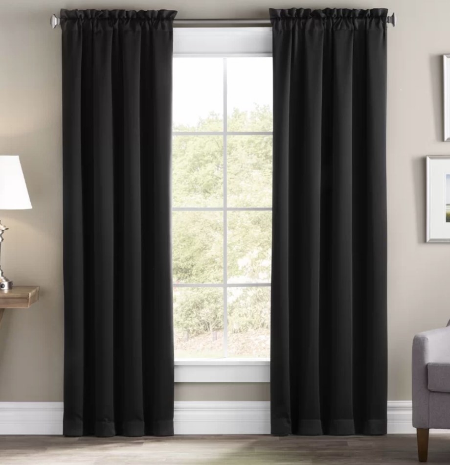 A set black, blackout curtains hanging from a rod over a window in a living room