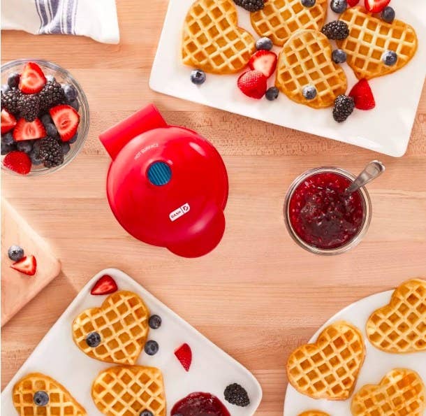 The waffle maker is being used to bake heart-shaped waffles, which are plated with strawberry jam and mixed berries