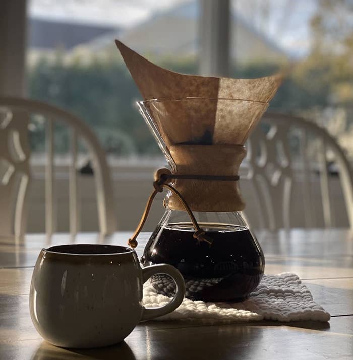 the coffee maker on a table in front of a window