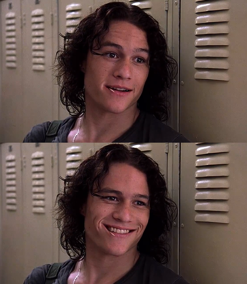 Heath Ledger in 10 Things I Hate About You; he is leaning against school lockers while looking at someone and smiling