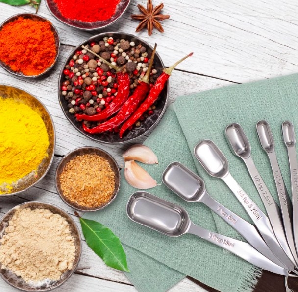 The six measuring spoons are arranged in a fanlike display next to bowls of various spices