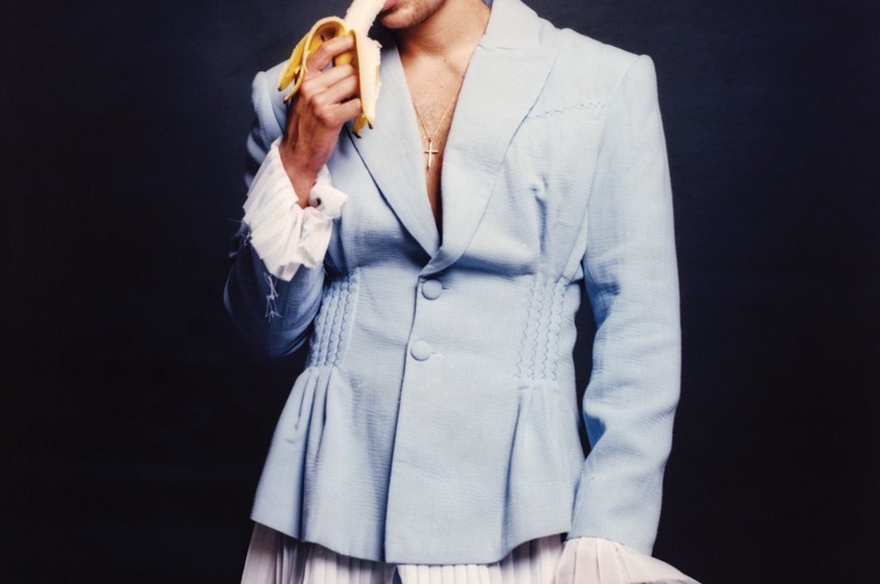 One Direction's Harry Styles eats a banana while dressed in a pastel blue suit.