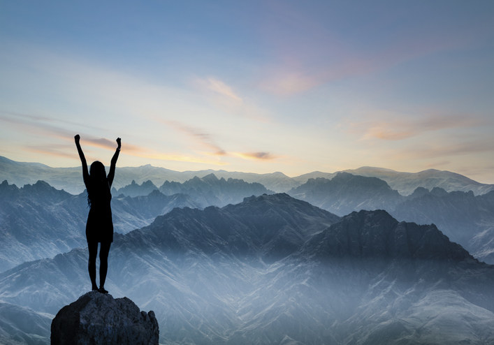 Woman standing on mountaintop with her arms in air triumphantly